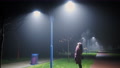 Girl Looks Up At The Bright White Light From A Lamppost. Inhales Steam At Night