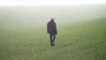 A Man With A Black Coat Walking Through Hail And Rain Storm On Grass Field.